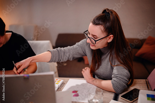 Two artists engage in a collaborative discussion over a watercolor palette, with one offering guidance as they navigate the hues together. photo