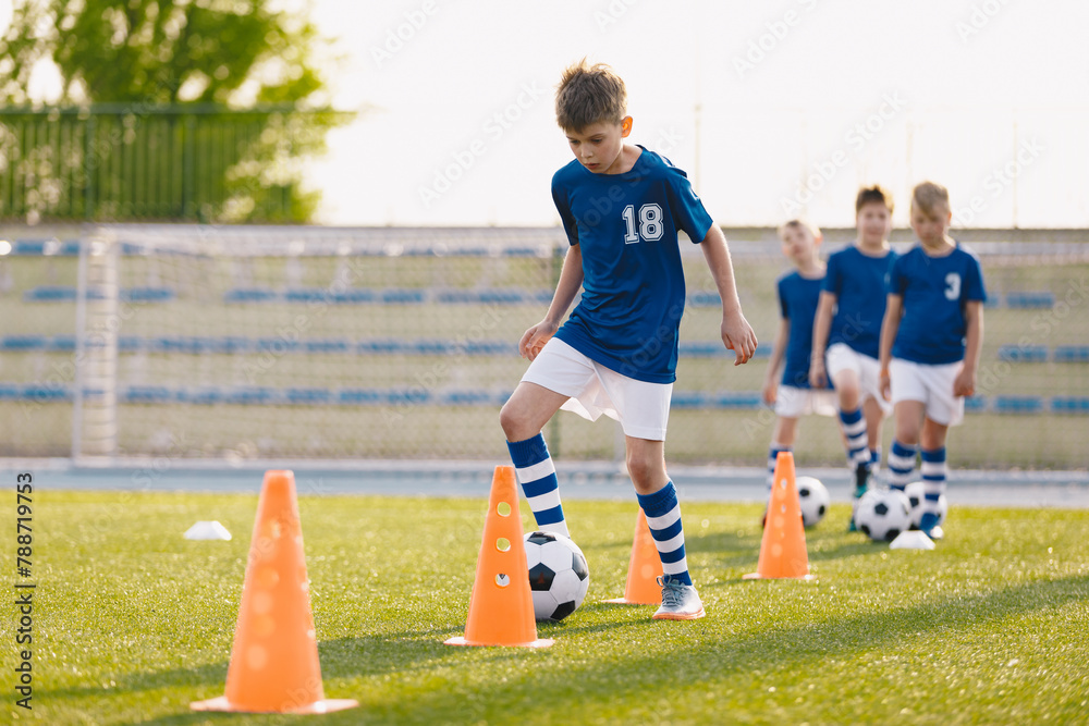 Fototapeta premium Happy Boys on Soccer Training Slalom Drill. School Kids Practicing European Soccer on the Grass School Field. Soccer Training - Warm Up and Slalom Drills