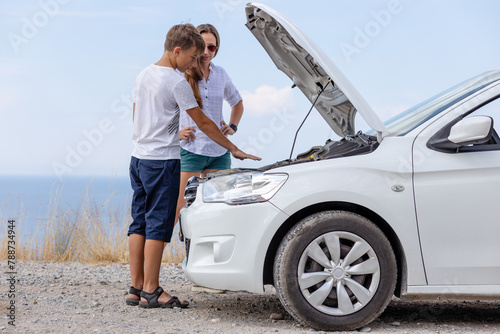Young woman with her son standing at broken down car with hood up having trouble with her vehicle