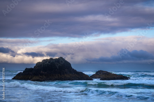 Sunset view of rock formations and pounding surf at Arch Cape, Oregon.  Dramatic clouds shroud two large rocks on the Oregon coast near Cannon Beach on the Pacific Oregon.