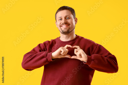 Handsome man making heart gesture on yellow background