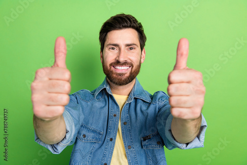 Photo of good mood handsome guy wear denim jacket showing you two thums up empty space isolated green color background photo