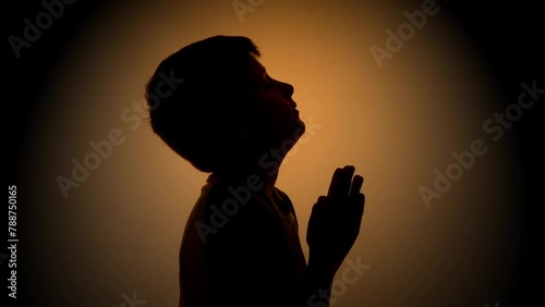 A young boy is praying to God above with his hands in a shadow with light for a Christianity faith concept or bible school idea.