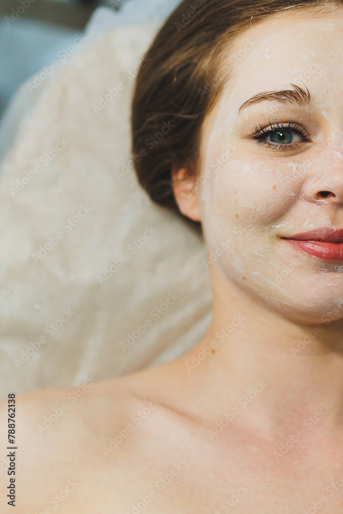 Naklejka premium Close-up of a young woman's face during a facial cleansing procedure in a beauty salon. A beautician in black gloves wipes a client's face with a napkin. Therapeutic facial skin care.