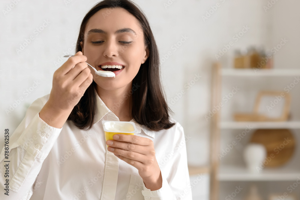 Happy young woman eating tasty yoghurt in kitchen, closeup Happy young woman eating tasty yoghurt in kitchen, closeup