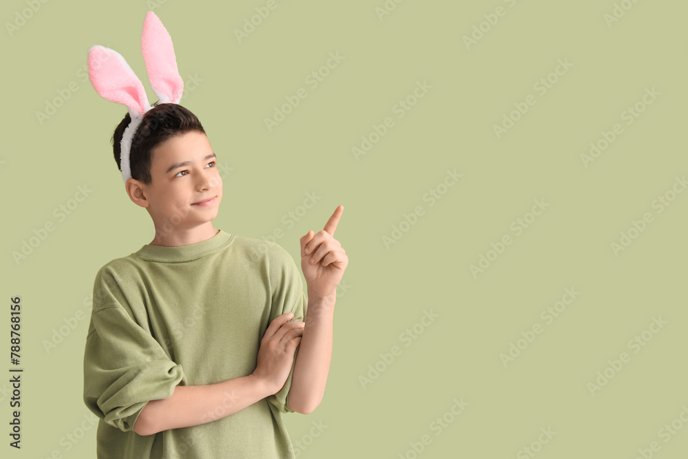 Little boy in bunny ears pointing at something on green background. Easter celebration Little boy in bunny ears pointing at something on green background. Easter celebration