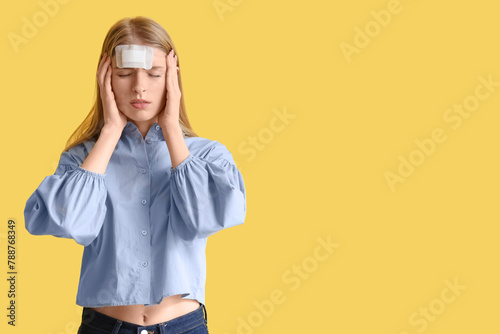 Young woman with brain concussion and medical patch on yellow background