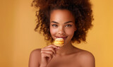 Beautiful smiling young african american woman holding a macaron on a yellow background