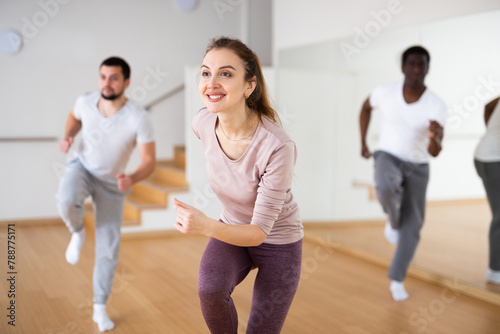 Cheerful woman dancing aerobic dance to warm up during group fitness training in studio.