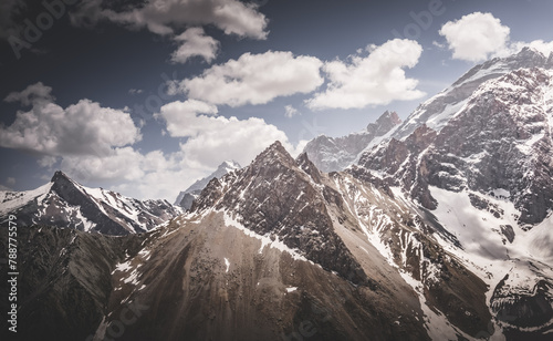 Panoramic landscape in the mountains with rocks and scree, with grass glades, snow and glaciers on a sunny summer day in the Fann Mountains in Tajikistan with mountain ranges