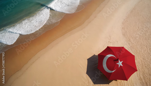 Fototapeta Naklejka Na Ścianę i Meble -  An aerial vista of a sandy beach with gentle ocean waves, featuring a beach umbrella adorned with the Turkey flag. Ideal for Turkey tourists seeking seaside relaxation
