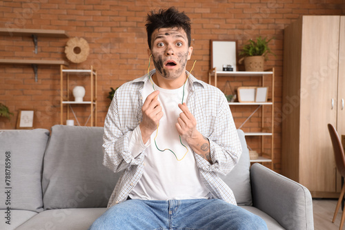 Canvas Print Electrocuted young man with burnt face and wire sitting on sofa at home