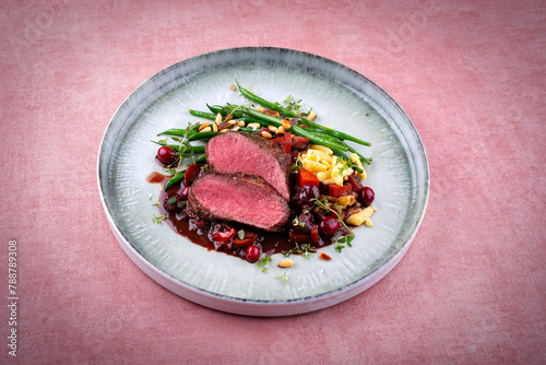 Traditionally roasted saddle of venison fillet with spätzle, vegetable and fruits in chocolate red wine sauce served as close-up on a Nordic design plate with copy space