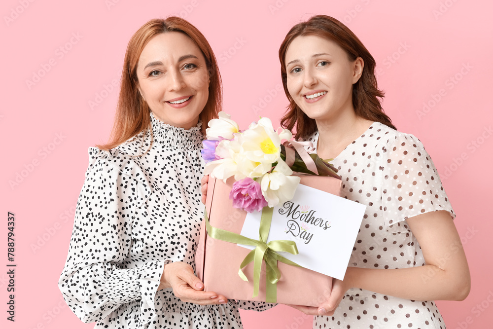 Beautiful mature woman with her daughter holding gift box, greeting card and bouquet of tulips on pink background. Mother's Day celebration Beautiful mature woman with her daughter holding gift box, greeting card and bouquet of tulips on pink background. Mother's Day celebration