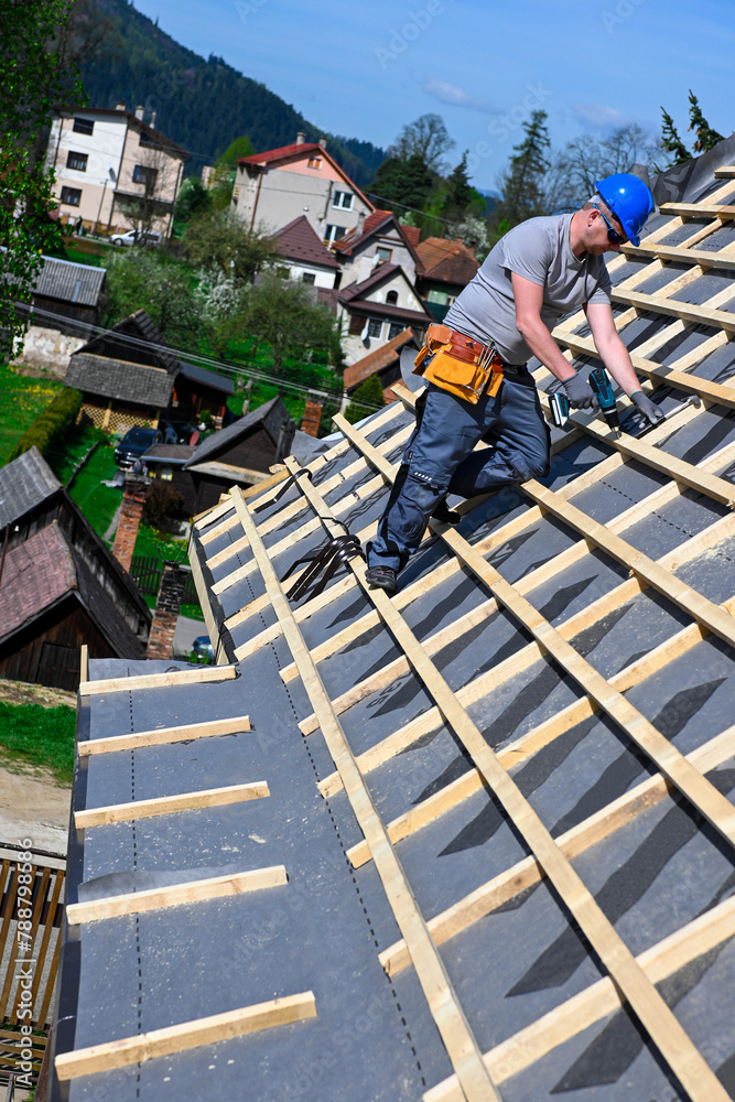 Repair and replacement of the old roof with a new one. Construction worker in protective clothing standing on roof with tools Repair and replacement of the old roof with a new one. Construction worker in protective clothing standing on roof with tools