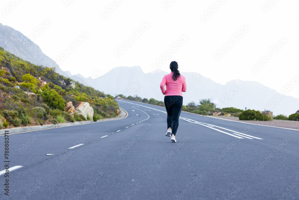 Biracial female hiker wearing a pink top and black leggings, jogging on a road with copy space Biracial female hiker wearing a pink top and black leggings, jogging on a road with copy space