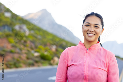 Biracial female hiker standing on mountain road, smiling, with copy space photo