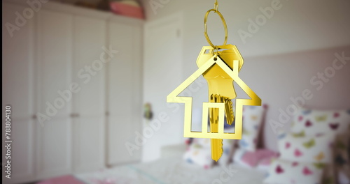 A golden house-shaped keychain hanging in focus with blurred bedroom background
