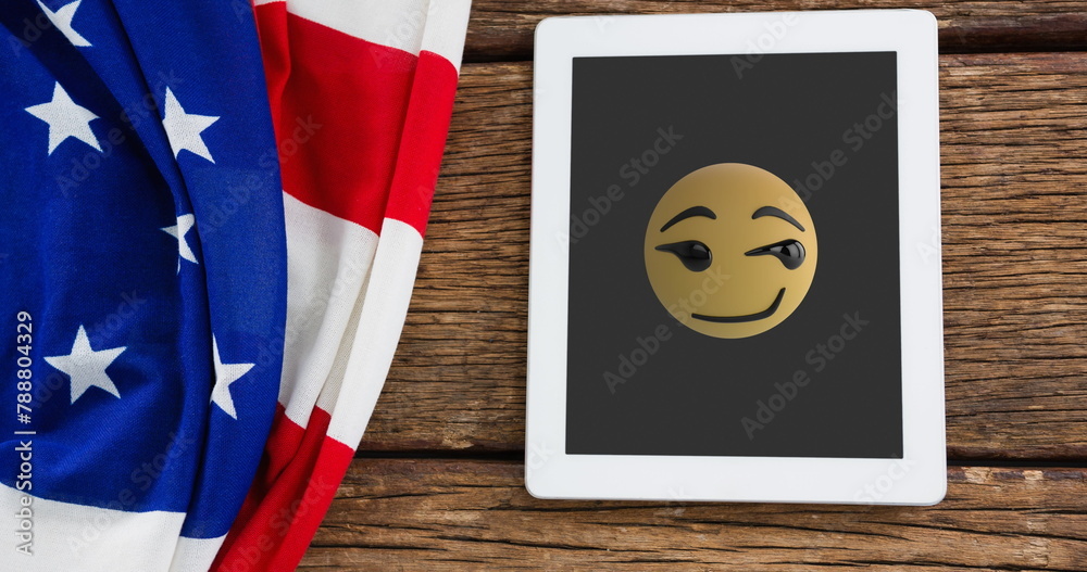 Naklejka premium A tablet displaying winking emoji rests beside American flag
