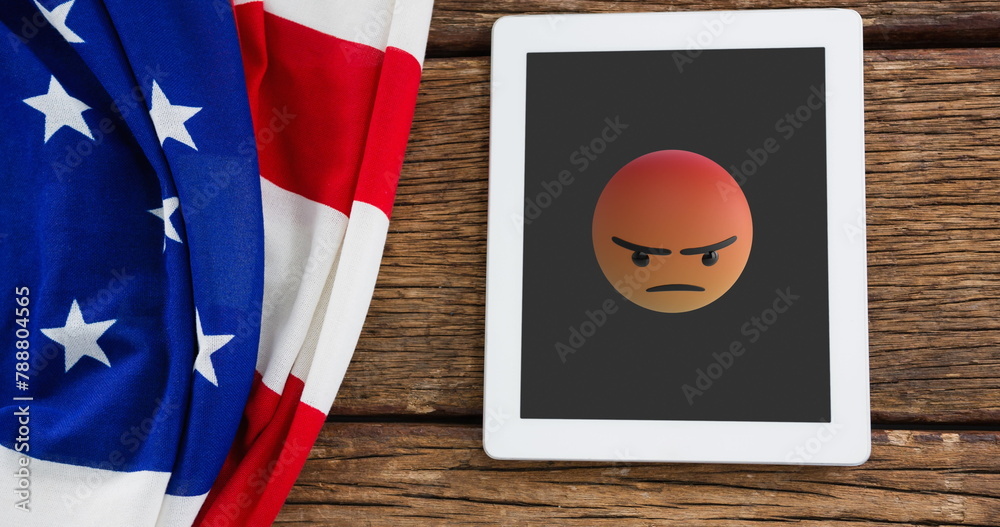 Naklejka premium A tablet displaying angry emoji rests beside an American flag