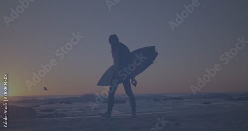 Caucasian young adult walking on beach, holding surfboard