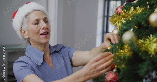 Caucasian senior woman with gray hair is decorating Christmas tree