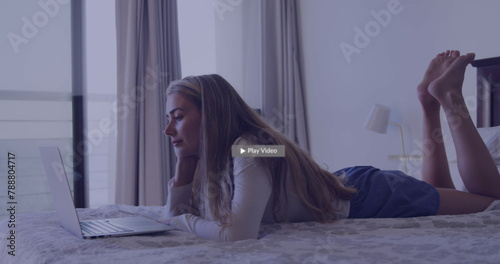 Caucasian young woman lying on bed, looking at laptop