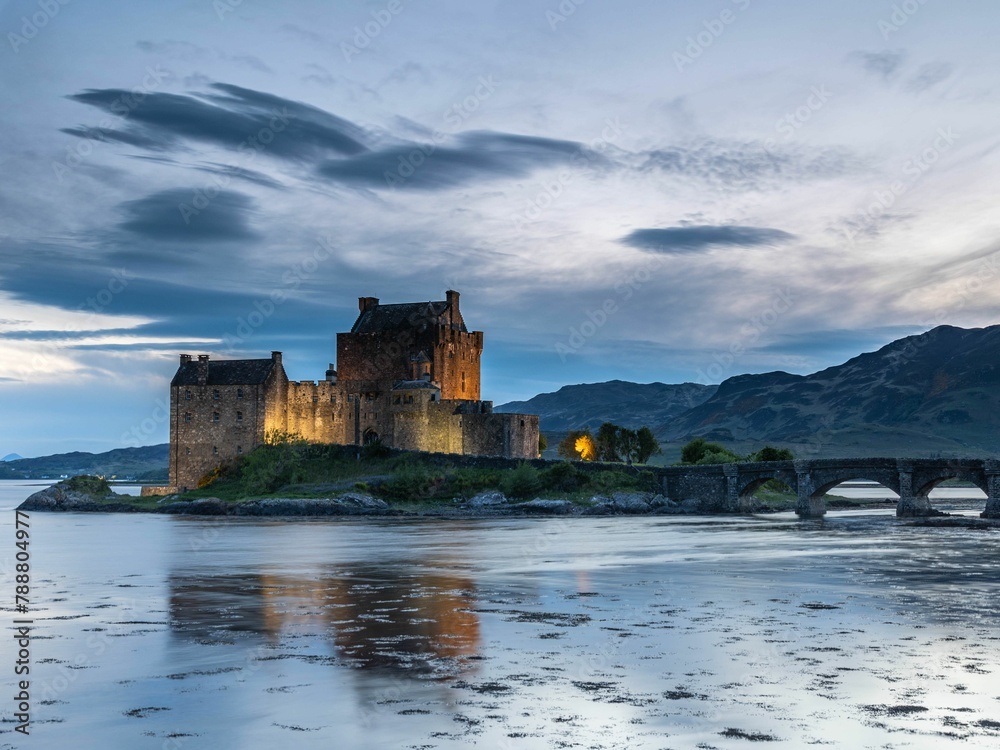 Eilean Donan Castle at sunset on water with rocks in foreground