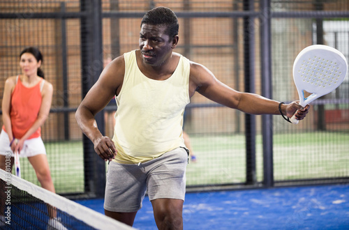 Sporty afro american man in yellow t-shirt playing padel tennis indoor