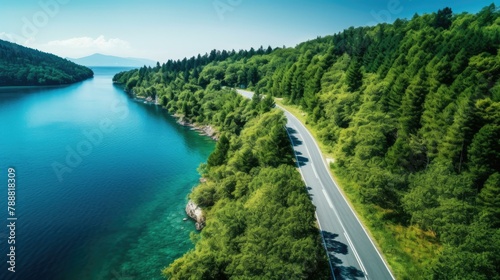 Curving road through the countryside along a lake on a sunny day with blue sky and green trees.