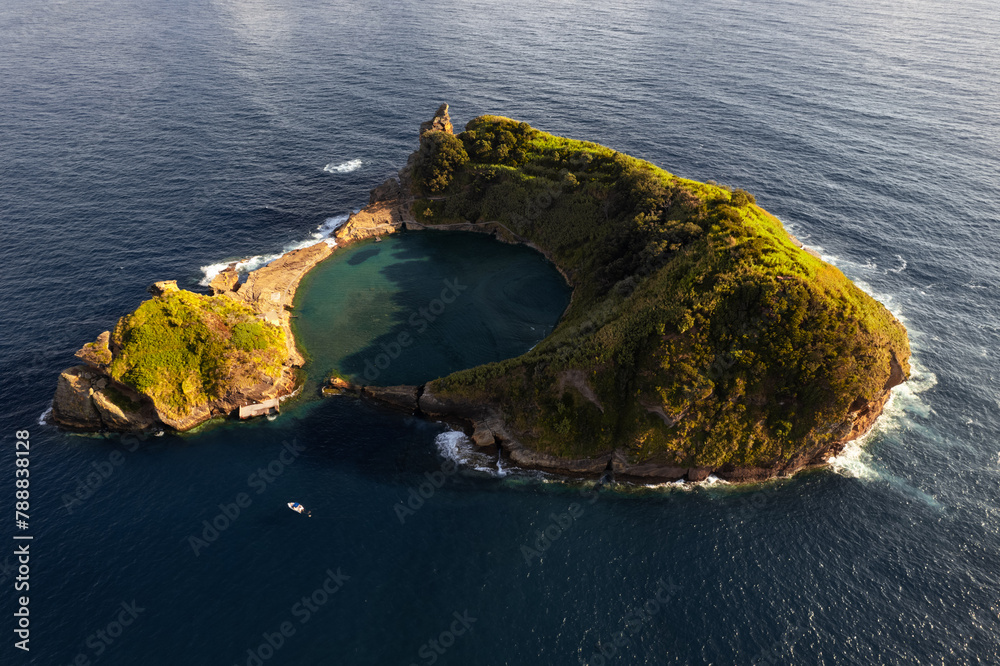 Fototapeta premium Picturesque volcanic islet in wavy ocean on sunny day
