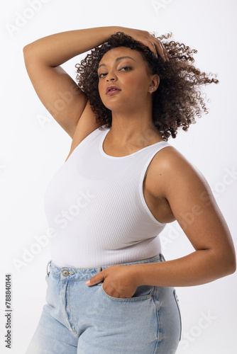 Biracial young female plus size model with curly brown hair posing confidently on white background, 