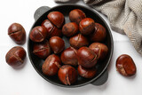 Fresh edible sweet chestnuts in frying pan on white tiled table, flat lay