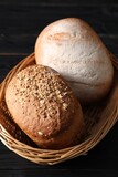 Wicker basket with fresh bread on black wooden table, closeup