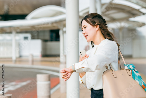 Obraz na plátně 駅・ターミナル・バス停で腕時計で時間を確認する若いビジネスウーマン（遅刻・遅れる・焦る・イライラ）