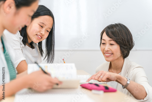 塾で先生に質問する小学生高学年のアジア人の女の子と女性講師
