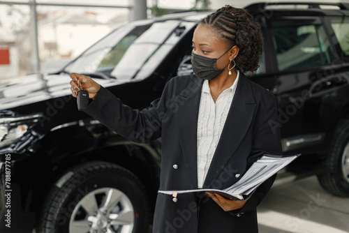 Black saleswoman standing at auto showroom and wearing a face mask