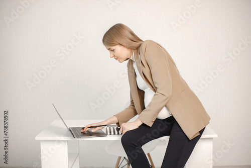 Pregnant lady typing on a laptop while sitting on desk in modern office