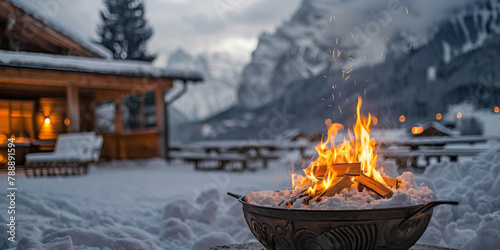 A cozy fire pit with wood in the background, set against a snowy mountain backdrop, offers warmth and comfort to guests during winter.