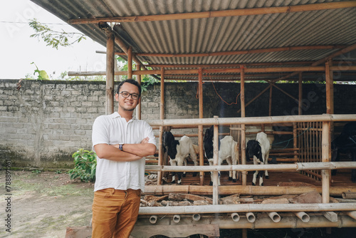 Excited young Asian man standing in front of traditional cage made from wood and bamboo in Indonesia rural area with goat inside
