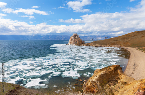 Scenic landscape of Baikal Lake in May. View of famous Shamanka rock - natural landmark of Olkhon Island and ice drift in Khuzhir bay on sunny windy day. Beautiful landscape. Spring travel, recreation