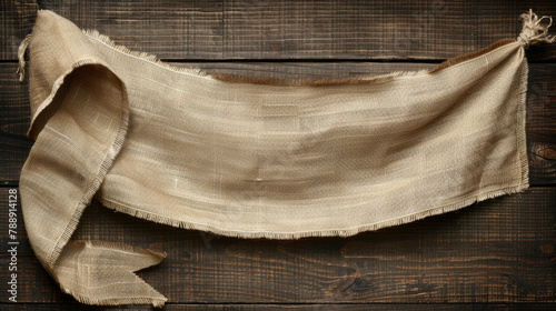 A large piece of cloth with a frayed edge is hanging on a wooden surface. The cloth is brown and has a rustic feel to it. The frayed edge gives the cloth a vintage and worn appearance
