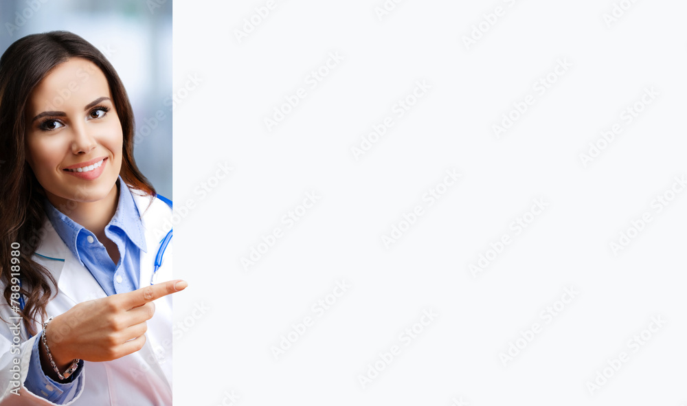 Portrait image of happy smiling female doctor pointing blank signboard with copy space empty area for ad slogan text. Young brunette beautiful woman in medical, clinic, healthcare concept