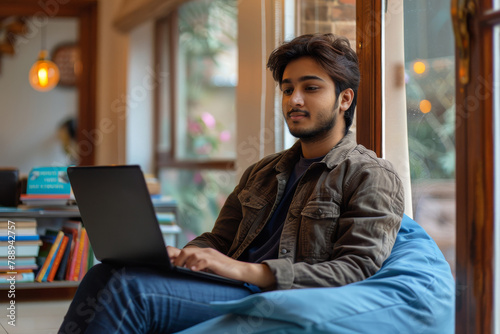 A man is sitting on a blue bean bag chair and using a laptop Free Download A man is sitting on a blue bean bag chair and using a laptop - GFXLoad