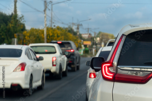 Cars on the road heading towards the goal of the trip. During the daytime traffic jam. Background beside road with tree and small city and electric pole