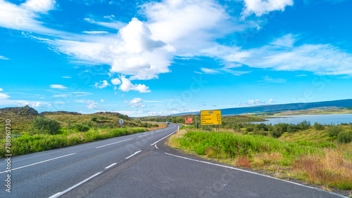 Panoramic over paved Ring road near Egilsstadir in Iceland with beautiful green landscape  lake and blue sky. Information board sign with distances to major cities.