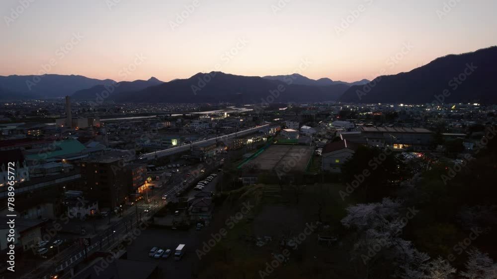 Dusk falls over Ueda city with mountain silhouettes, featuring a river cutting through the landscape. Shinkansen can be seen running through the city. Dusk falls over Ueda city with mountain silhouettes, featuring a river cutting through the landscape. Shinkansen can be seen running through the city.