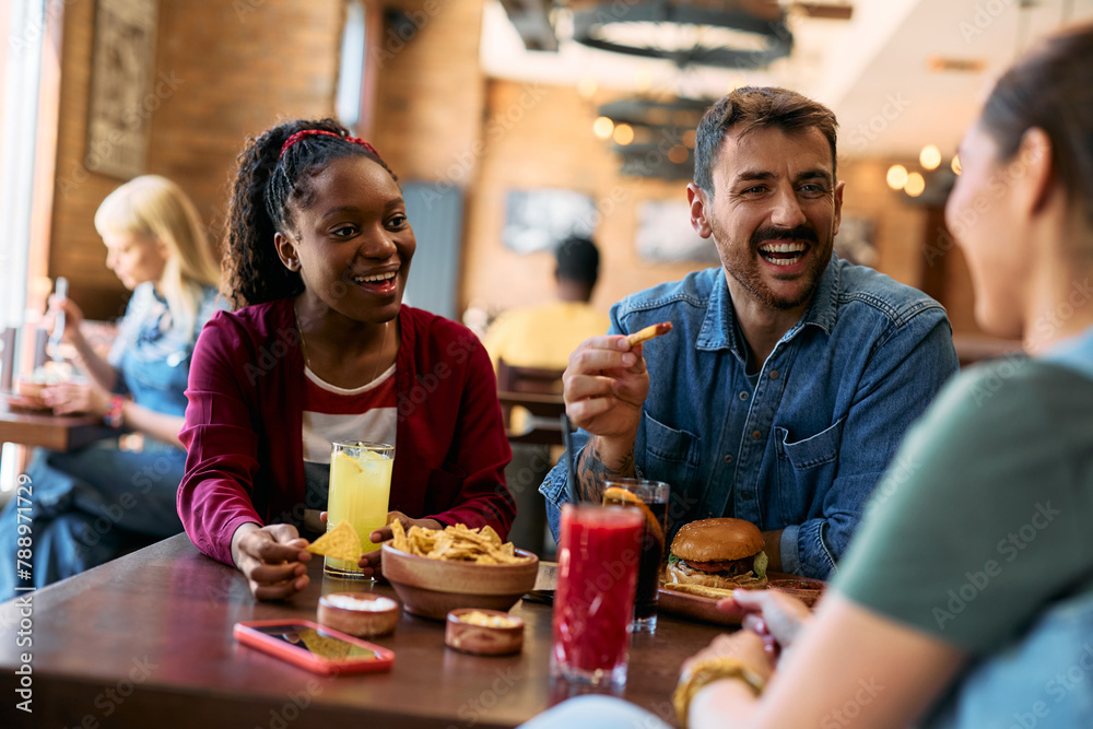Young happy man and his friends talking while eating in pub. Young happy man and his friends talking while eating in pub.