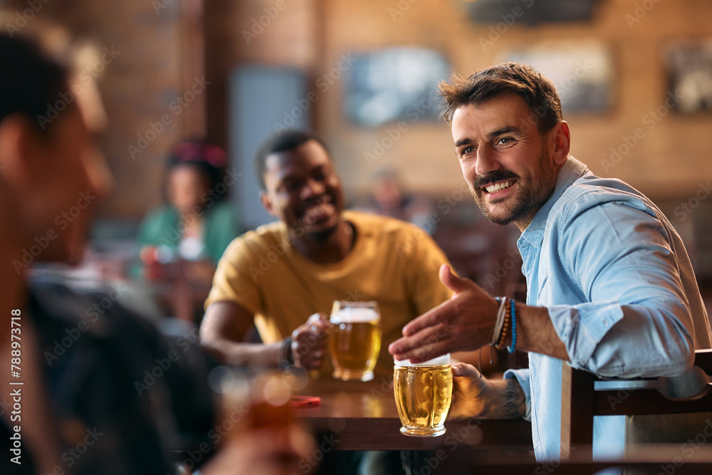 Happy man talking to his friends while drinking beer in pub.
