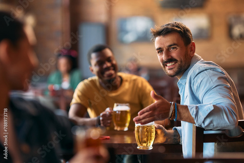 Happy man talking to his friends while drinking beer in pub. © Drazen